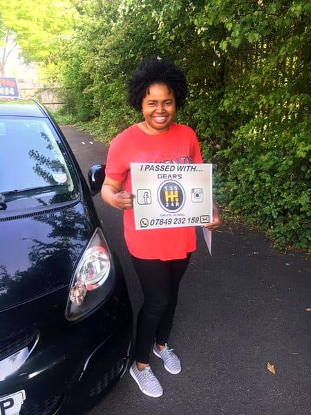 A beaming learner in a red T-shirt holds a Gears pass board beside a black Toyota Aygo