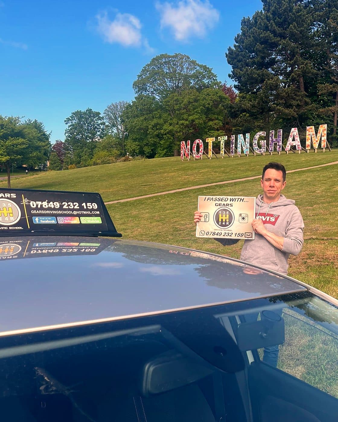 A learner holds a Gears pass board on a grassy hillside beneath giant NOTTINGHAM letters, with the Gears roof sign in the foreground