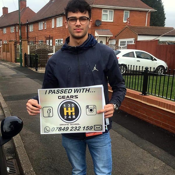 A learner in glasses holds a Gears pass board on a residential street