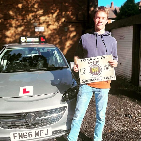 A smiling learner holds a Gears pass board beside a silver Vauxhall Corsa in the sunshine