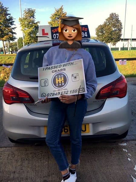 A learner, face covered by a graduate emoji, holds a Gears pass board behind a silver Vauxhall Corsa