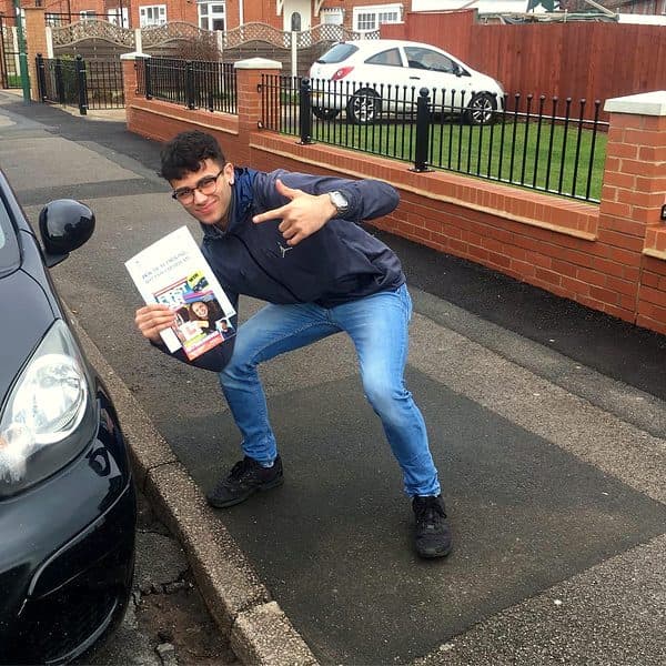 A learner strikes a celebratory pose with a pass certificate beside a black Toyota Aygo