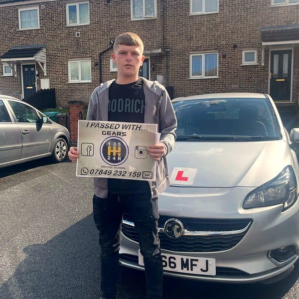 A young learner holds a Gears pass board in front of a silver Vauxhall Corsa outside brick houses