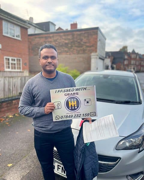 A learner holds a Gears pass board and a pass certificate beside a silver Vauxhall Corsa