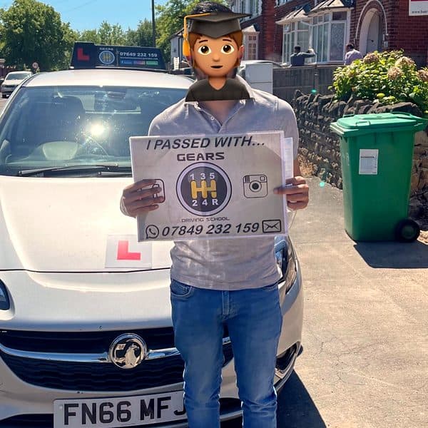 A learner, face covered by a graduate emoji, holds a Gears pass board in front of a silver Vauxhall Corsa