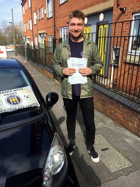 A smiling learner in a green jacket holds a pass certificate beside a black Toyota Aygo