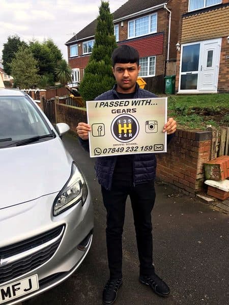 A young learner holds a Gears pass board beside a silver Vauxhall Corsa outside a semi-detached house