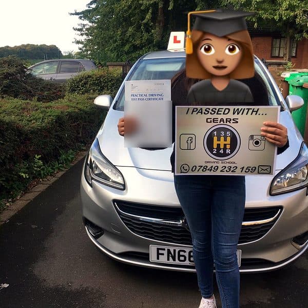 A learner, face covered by a graduate emoji, holds a Gears pass board and a pass certificate in front of a silver Vauxhall Corsa