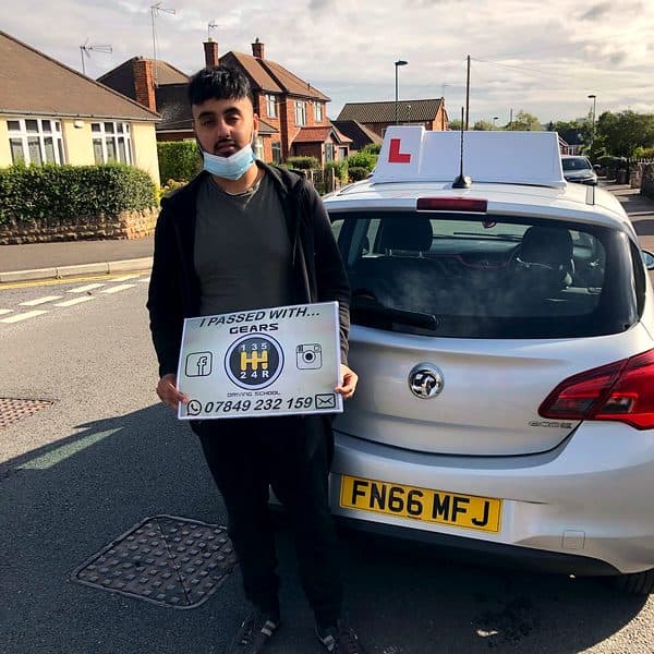 A learner holds a Gears pass board beside a silver Vauxhall Corsa with a Gears roof sign