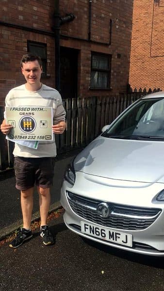 A learner holds a Gears pass board beside a silver Vauxhall Corsa on a quiet street