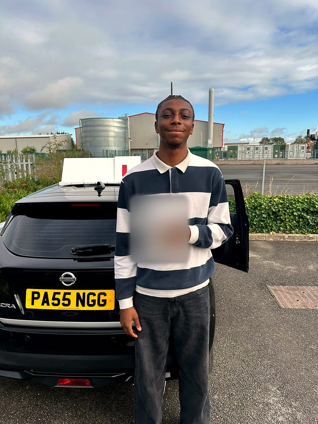 A smiling learner in a striped rugby shirt holds a pass certificate beside a black Nissan Micra