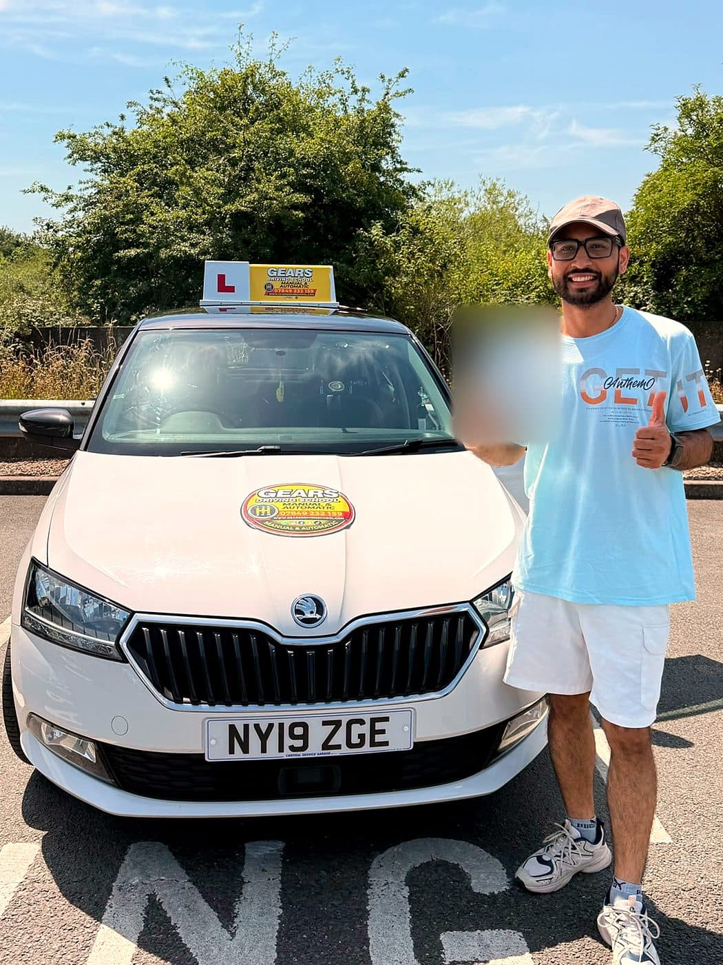 A smiling learner in a cap and glasses gives a thumbs up with a pass certificate beside a white Skoda Fabia