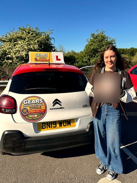 A smiling learner in a varsity jacket holds a pass certificate beside a white Citroën C3 with a red roof