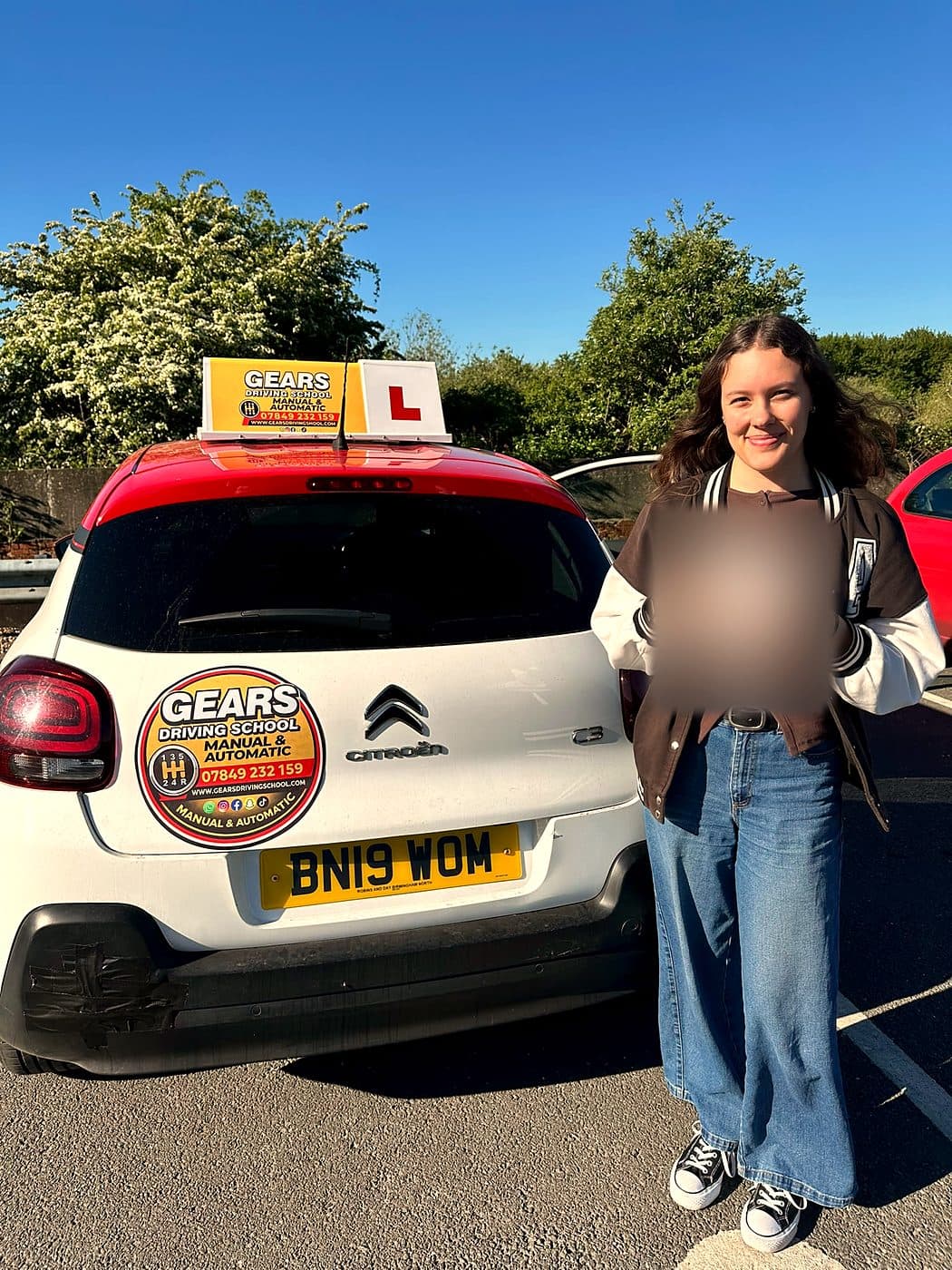 A smiling learner in a varsity jacket holds a pass certificate beside a white Citroën C3 with a red roof