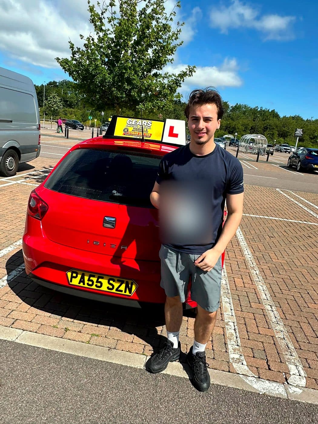 A learner in a navy T-shirt holds a pass certificate beside a red SEAT Ibiza on a sunny day