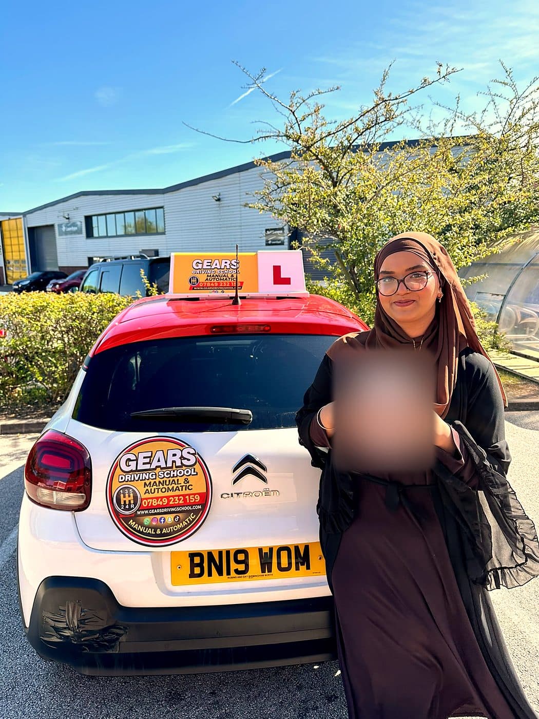 A learner in glasses and a brown hijab holds a pass certificate beside a white Citroën C3